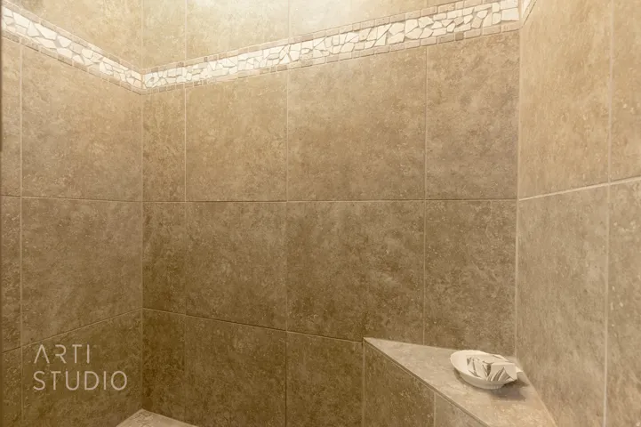 Tiled shower enclosure featuring a mosaic accent band, integrated corner shelf, and neutral-toned wall tiles