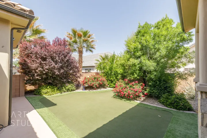 Private backyard featuring an artificial turf putting green, mature landscaping, and an extended concrete patio