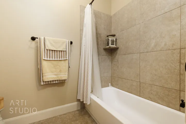 Bathroom featuring a white bathtub, large format stone-look tile surround, and a built-in corner shelf