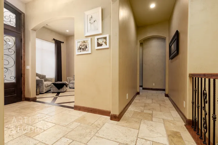 Travertine tile flooring throughout the entryway and hallway, featuring dark wood trim and arched doorways