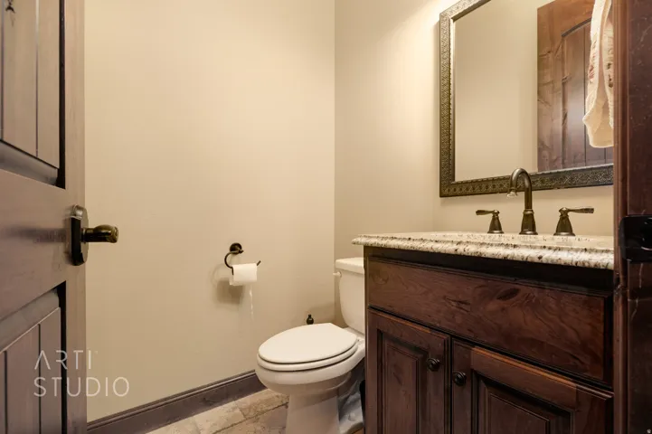 Bathroom featuring a wood-finish vanity with granite countertop, bronze-finish faucet, framed mirror, and tile flooring
