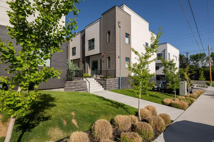 Modern multi-story exterior with contrasting light and dark siding, a prominent entryway staircase, and iron railings