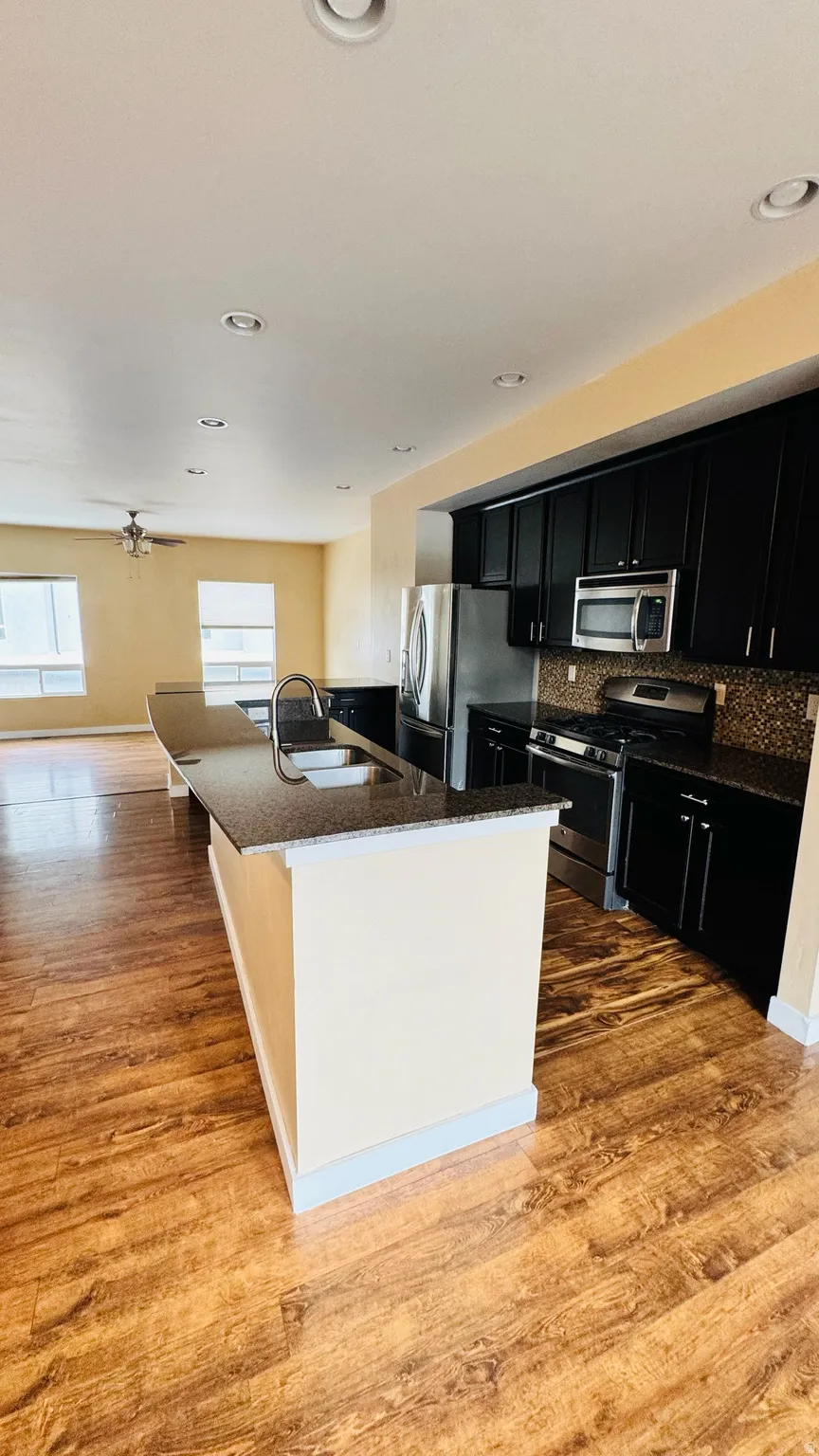 Kitchen featuring dark wood cabinetry, stainless steel appliances, a mosaic tile backsplash, and an extended island with a double basin sink