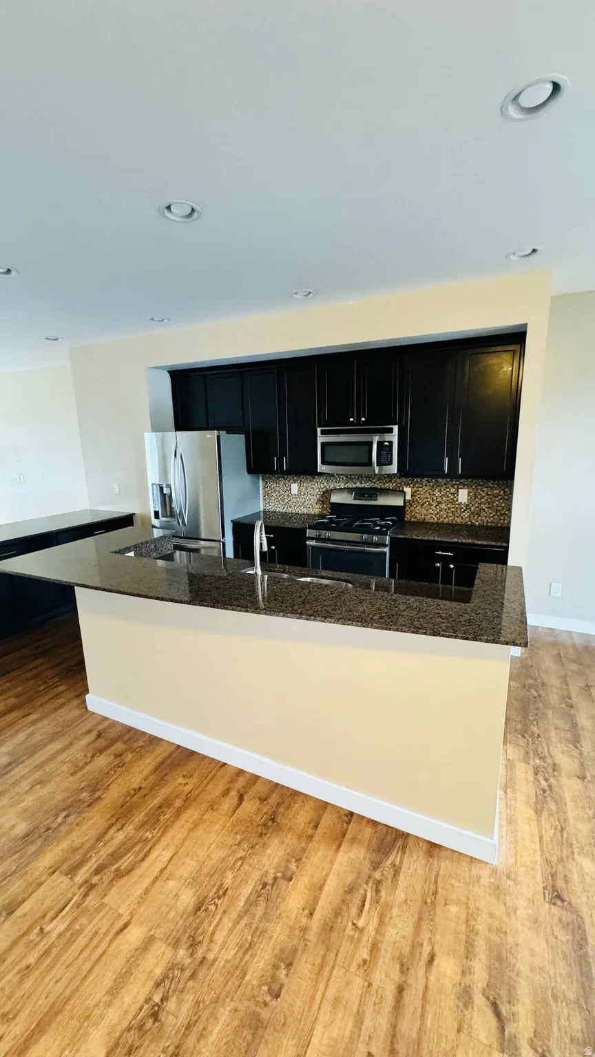 Kitchen featuring dark cabinetry, stainless steel appliances, a mosaic tile backsplash, and granite countertops