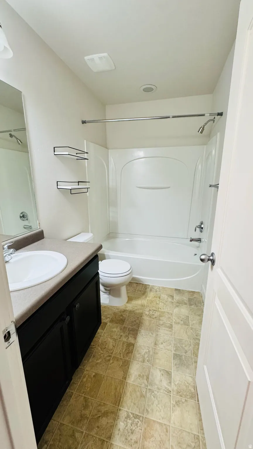 Full bathroom featuring a white tub/shower combination, dark wood-finish vanity with a single basin sink, light-toned countertop, and patterned floor tiling