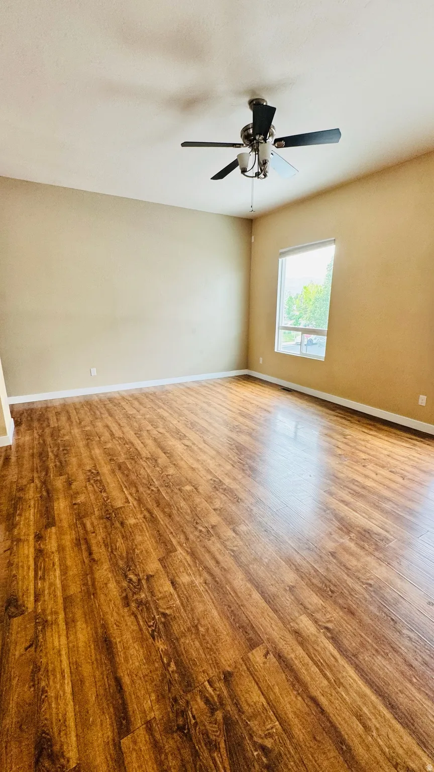 Spacious room featuring wood-finish flooring, a contemporary ceiling fan, and ample natural light from a large window