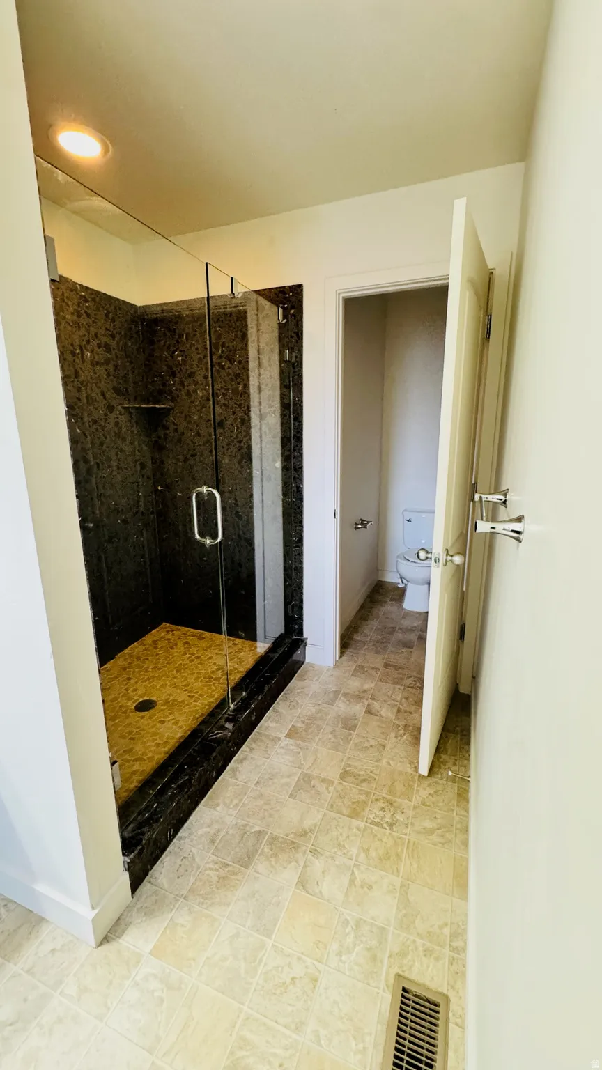 Walk-in shower with dark stone-finish walls, clear glass enclosure, and a light-toned shower pan