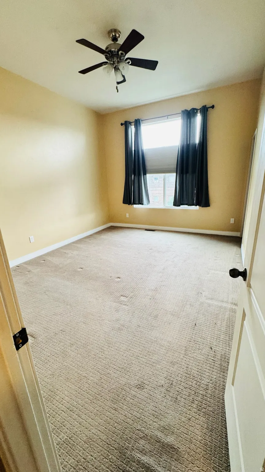 Spacious room featuring neutral carpeting, a single window, and a ceiling fan with integrated lighting