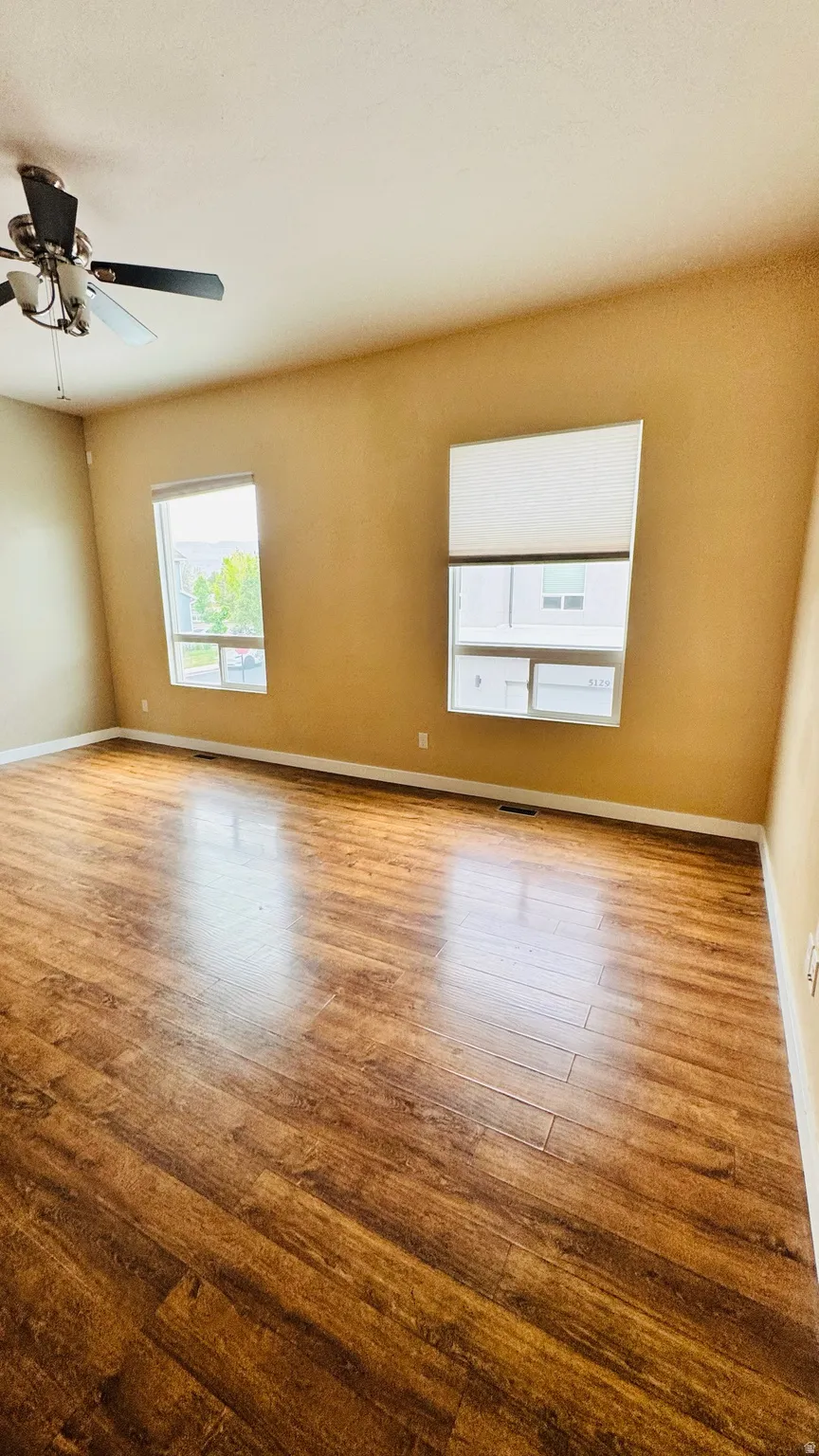 Spacious room featuring wood-finish flooring, two windows, and a ceiling fan with integrated lighting