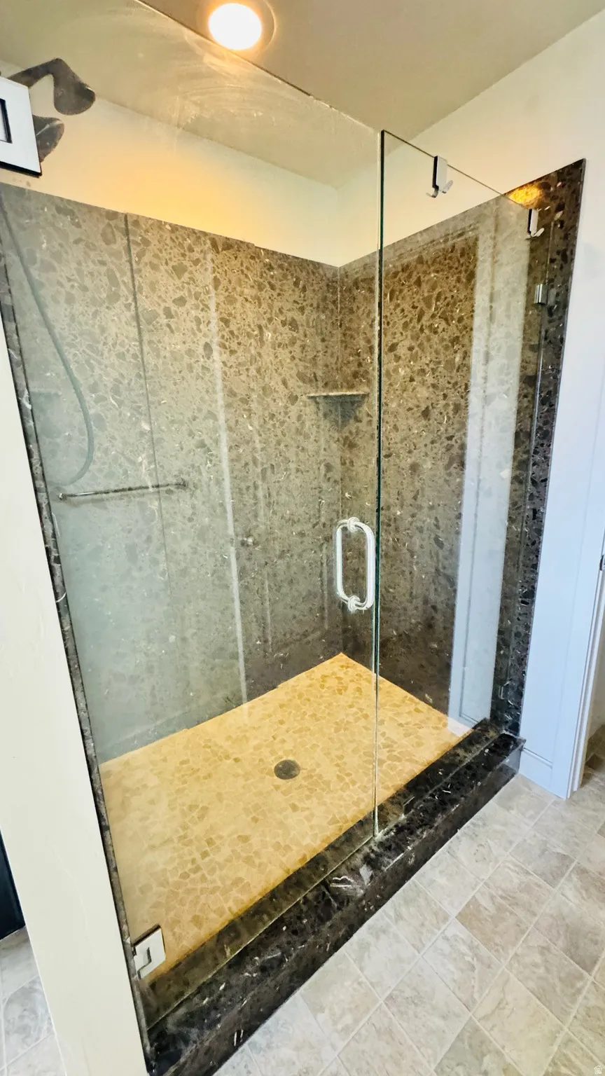 Glass-enclosed shower featuring speckled wall tile, a pebble-finish shower floor, and a dark stone curb