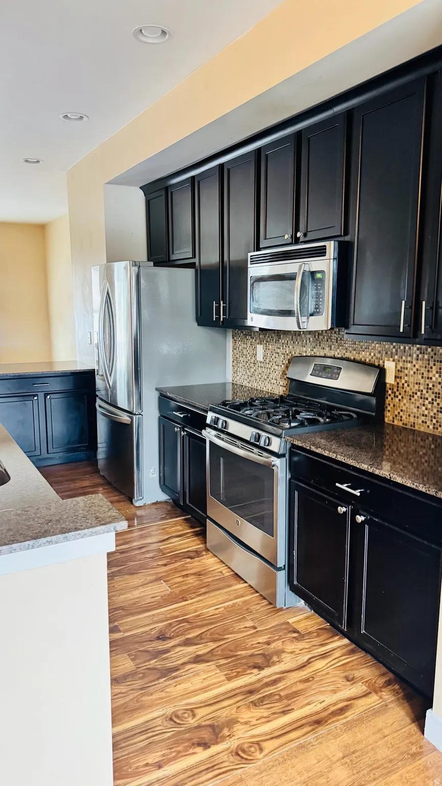 Kitchen featuring dark cabinetry, stainless steel appliances, mosaic tile backsplash, wood-finish flooring, and recessed lighting