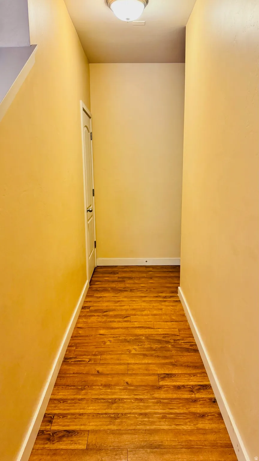Hallway featuring wood-finish flooring, light-toned walls, white baseboards, and a flush mount ceiling light