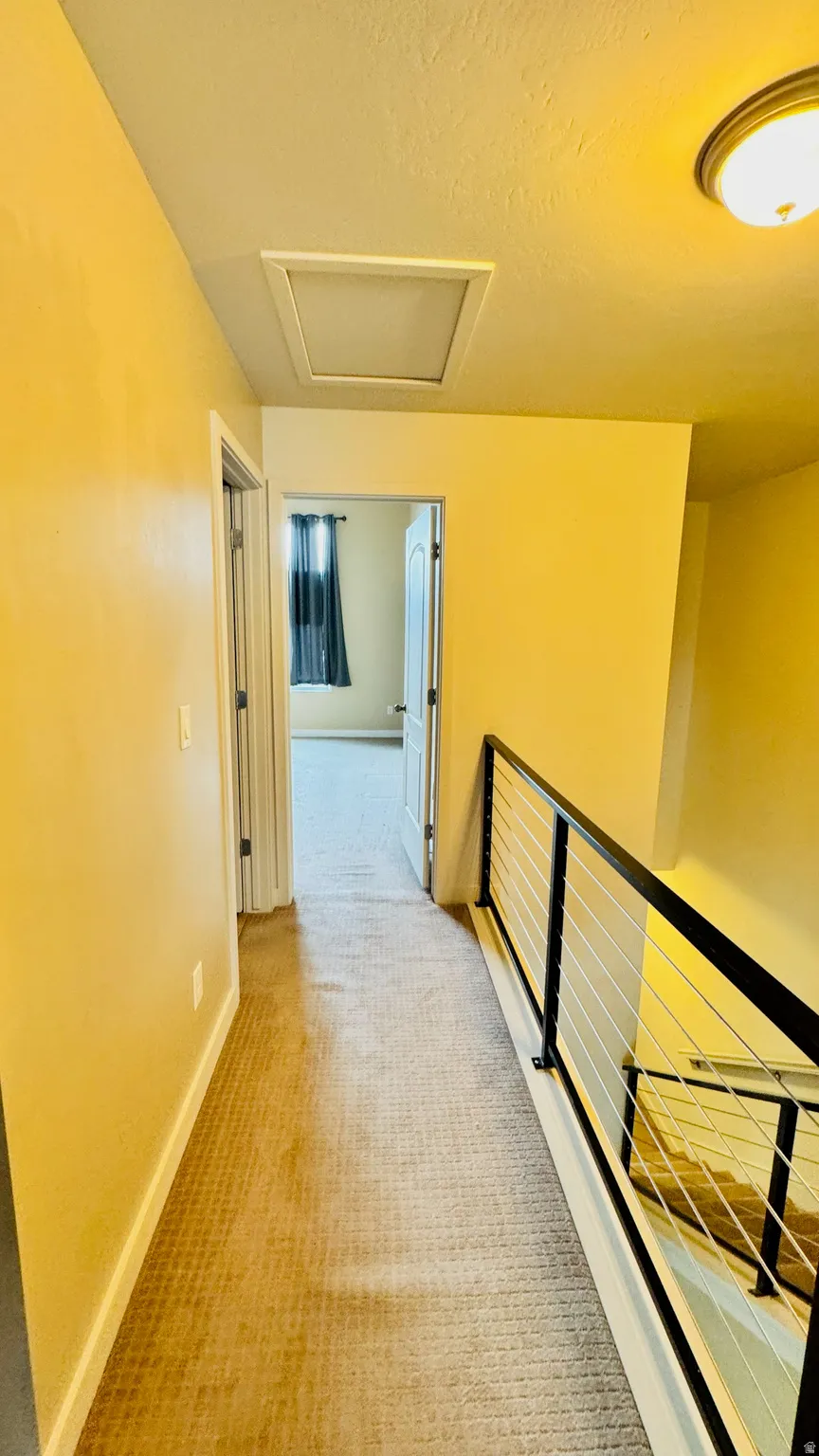 Carpeted hallway with a modern black and wire railing system, leading to a room with a window and dark curtains
