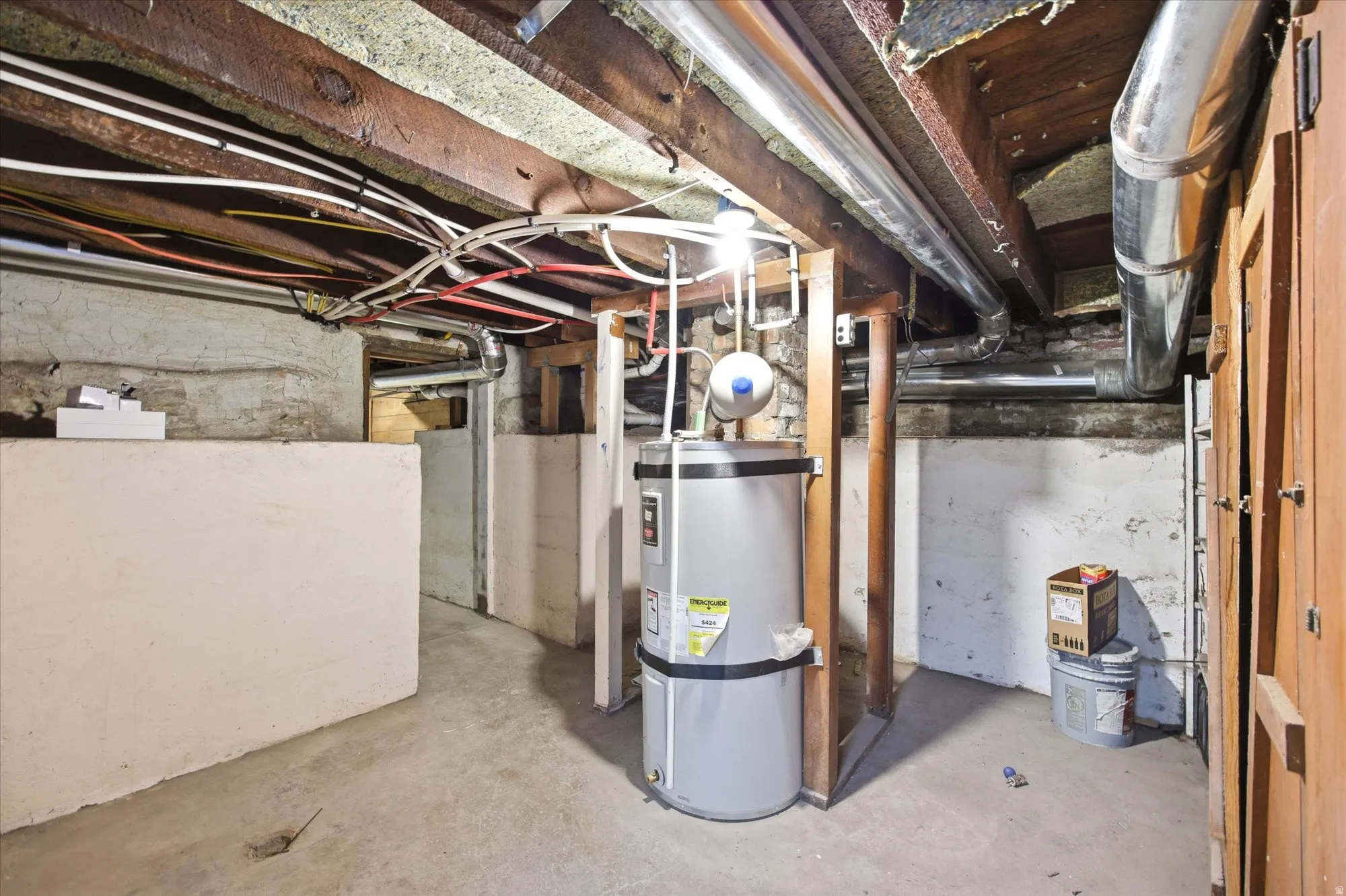 Utility room featuring a water heater, exposed ceiling joists, and various pipes and conduits