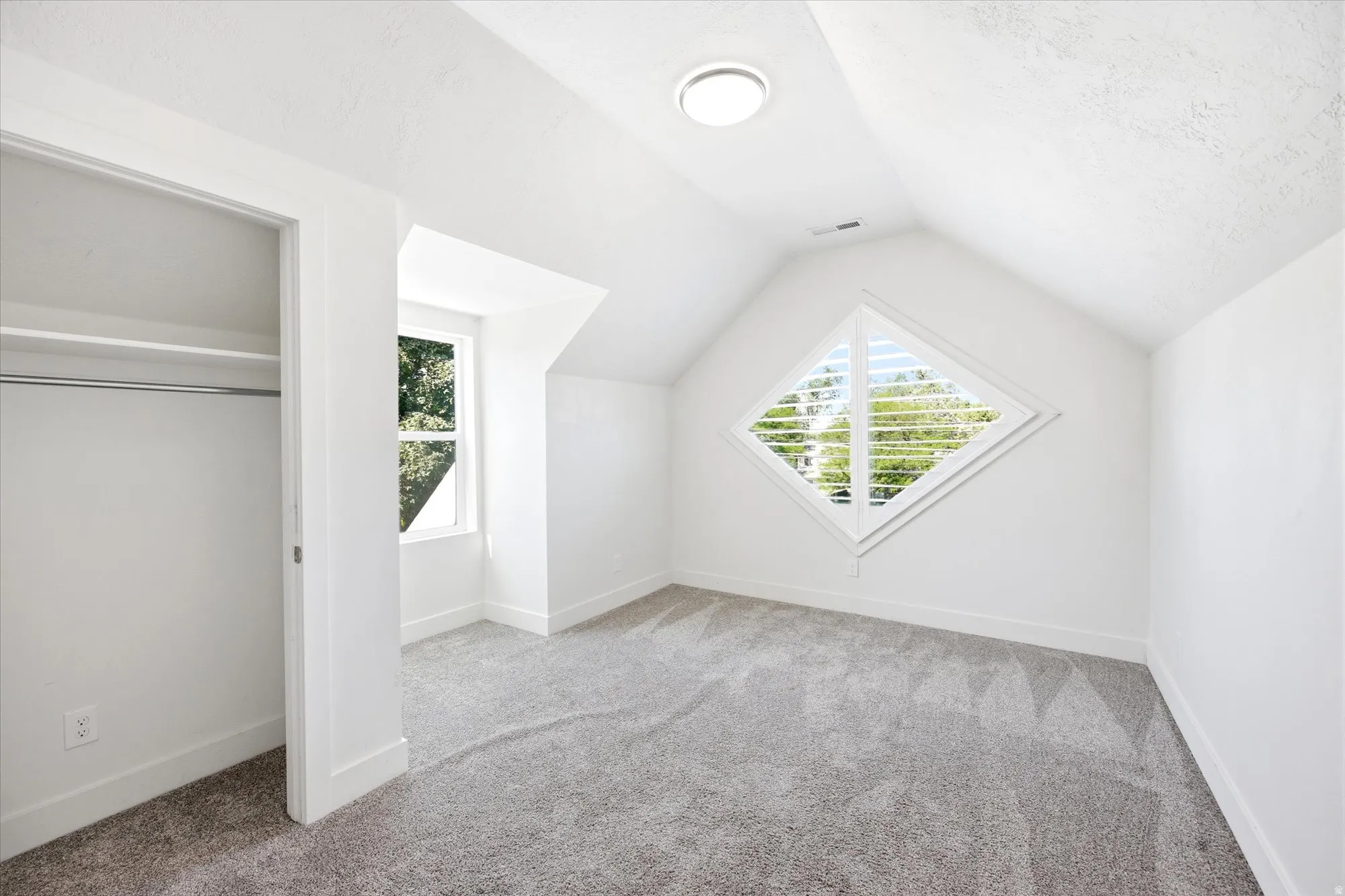 Attic room featuring a diamond-shaped window with plantation shutters, white walls, and gray carpet