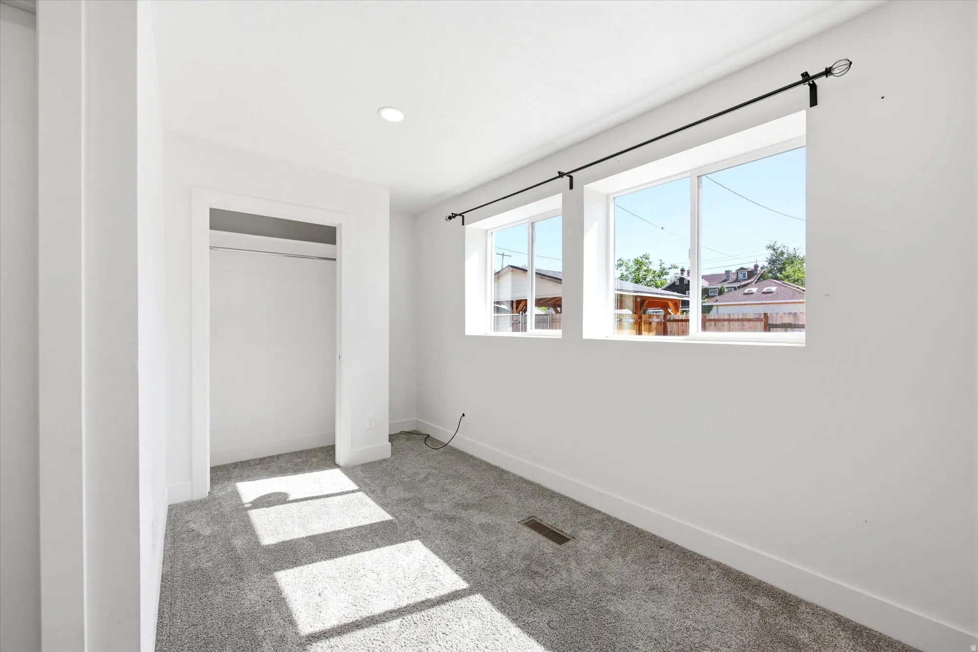 Bright room featuring two windows with dark curtain rods, recessed lighting, white walls, and gray carpet flooring