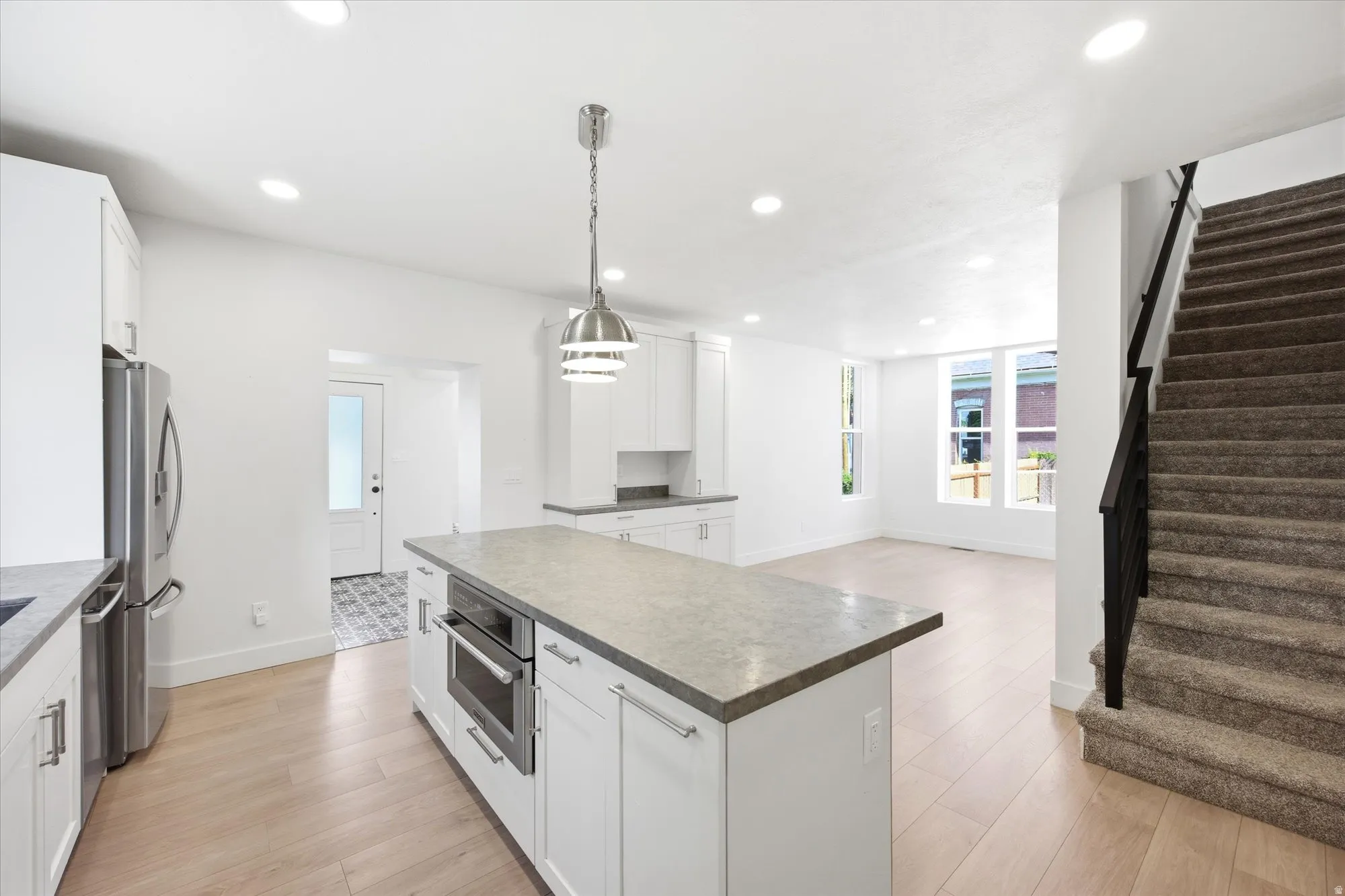 Open-concept kitchen and living area featuring light wood-finish flooring, recessed lighting, and a kitchen island with an integrated microwave