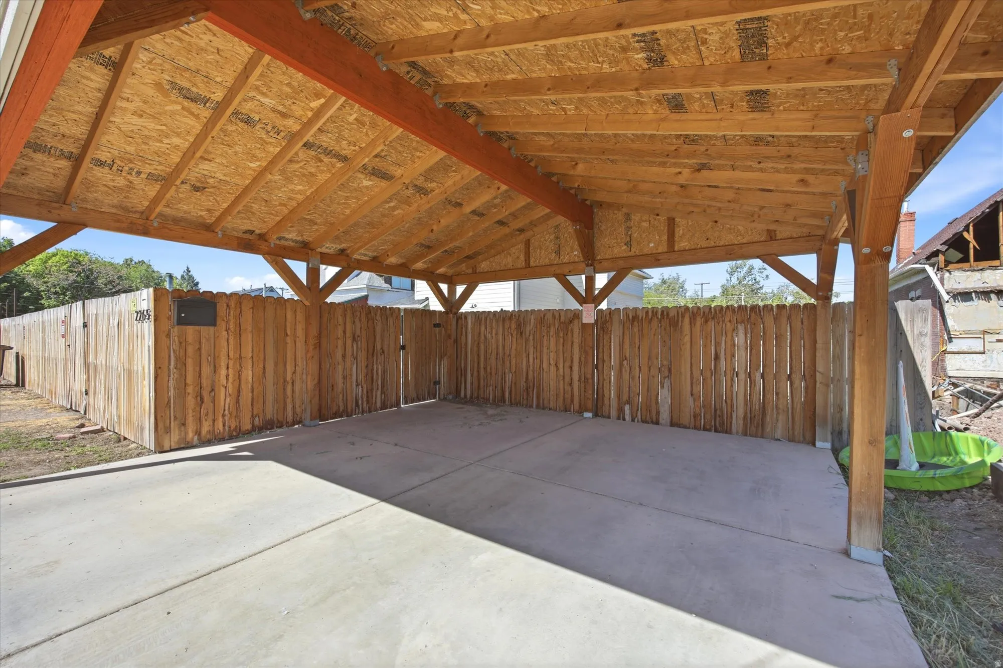 Covered carport featuring a wood-finish ceiling, exposed beams, and concrete flooring