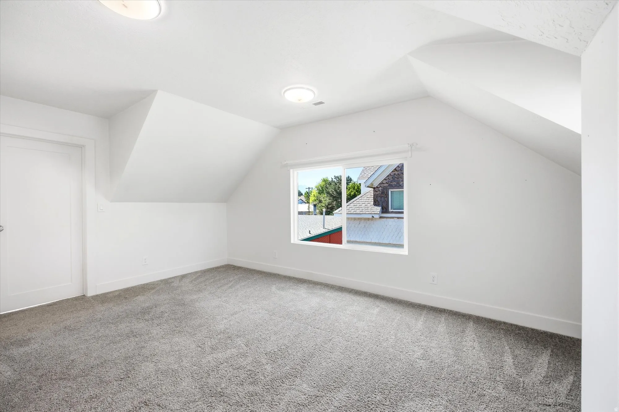 Room featuring sloped ceilings, a window with exterior views, light gray carpet, and white walls