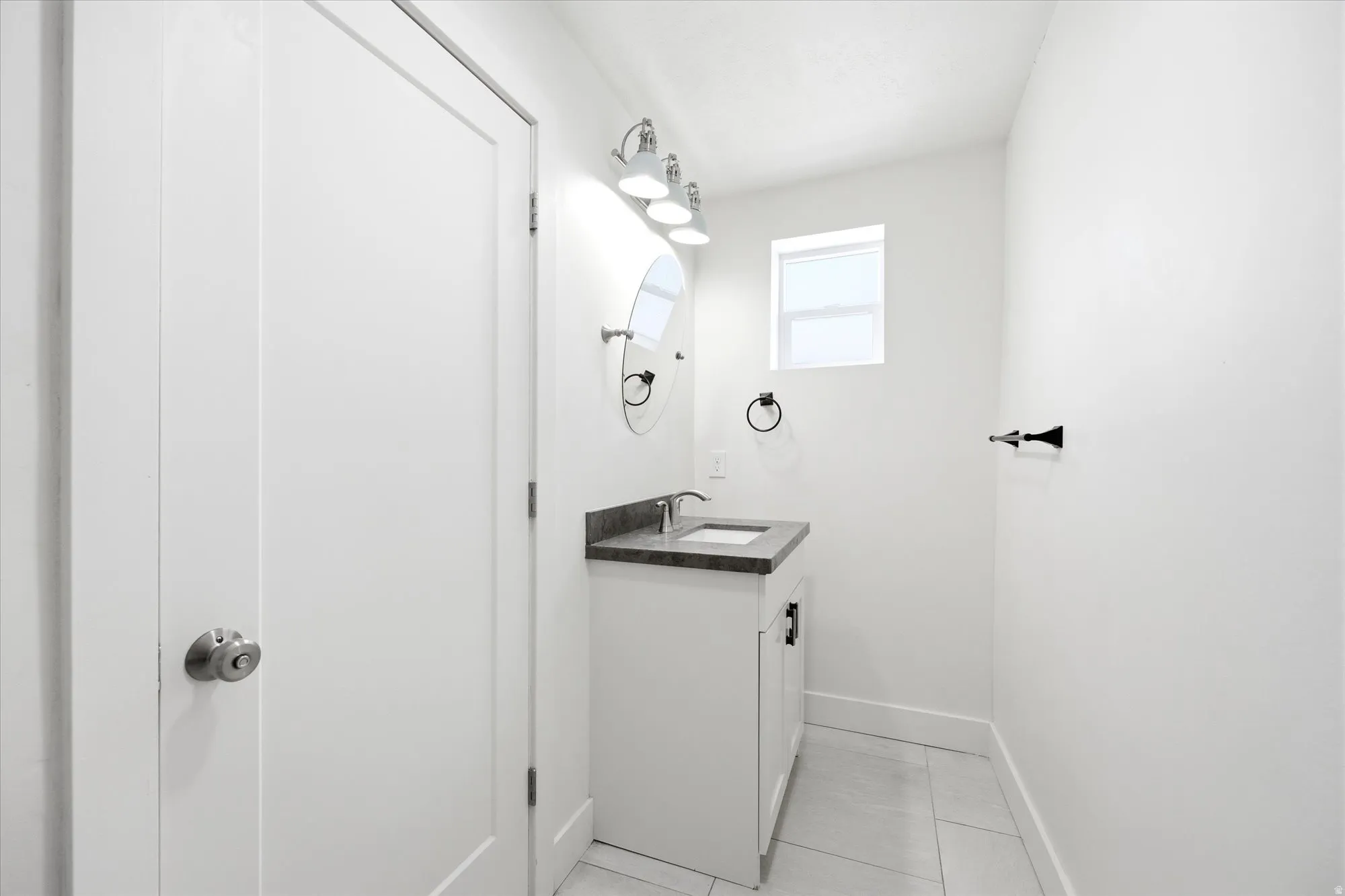 Modern bathroom featuring a white vanity with a dark countertop, an undermount sink, and a circular mirror