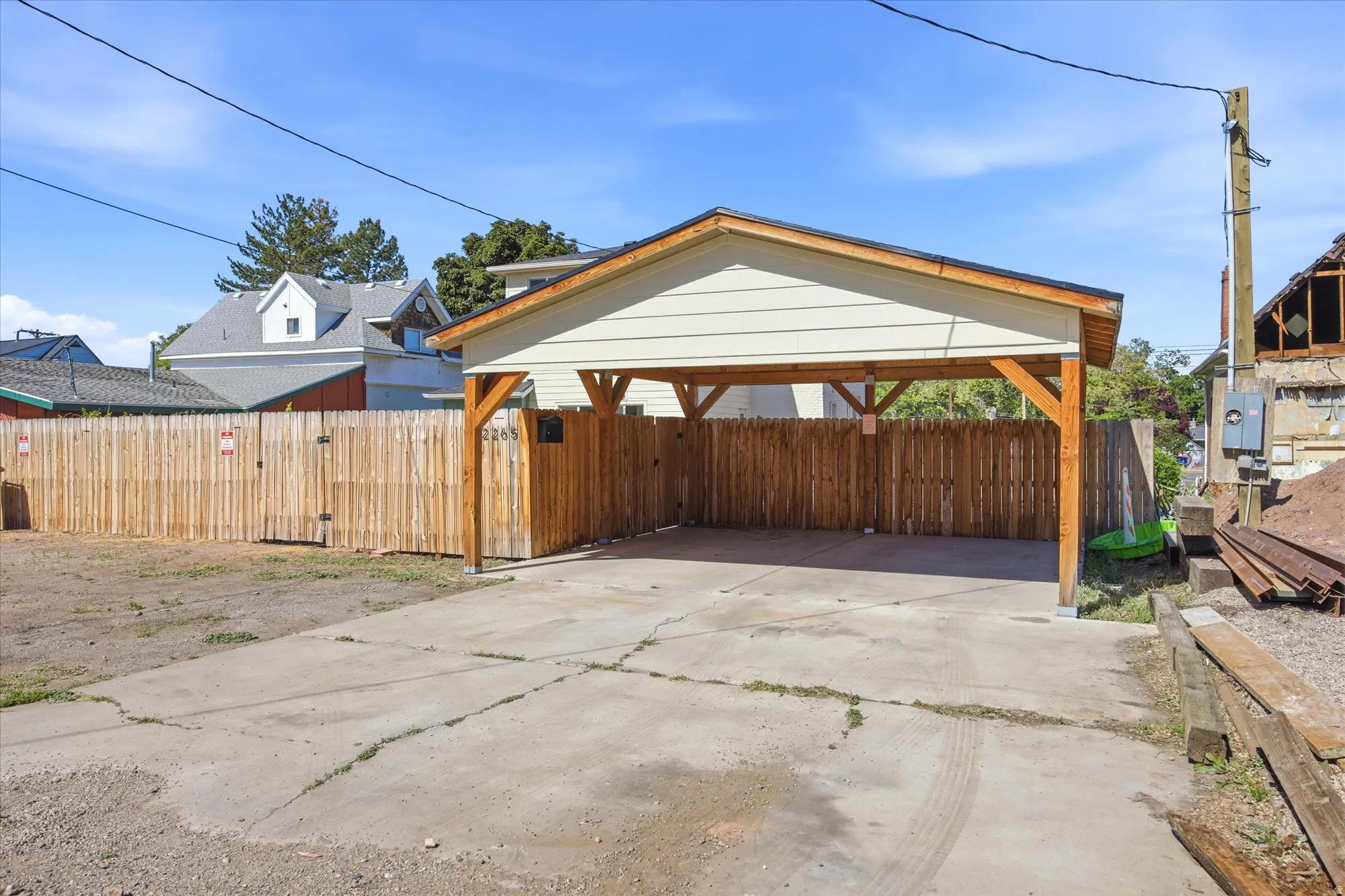 Covered carport with a concrete slab, featuring a wood-finish fence and a gate