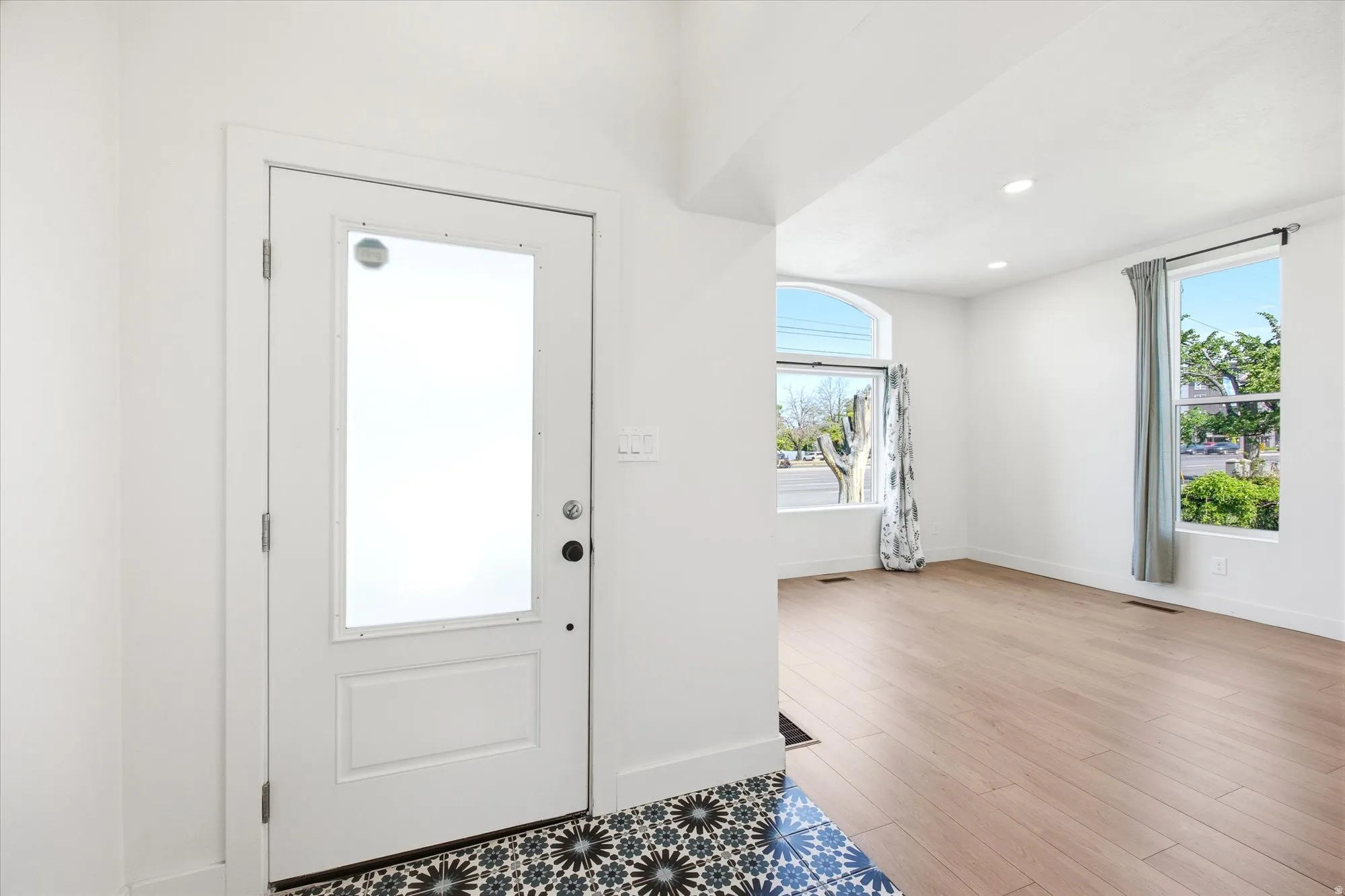 Entryway featuring patterned tile flooring, a white door with frosted glass, and seamless access to a room with light wood-finish flooring, recessed lighting, and multiple windows