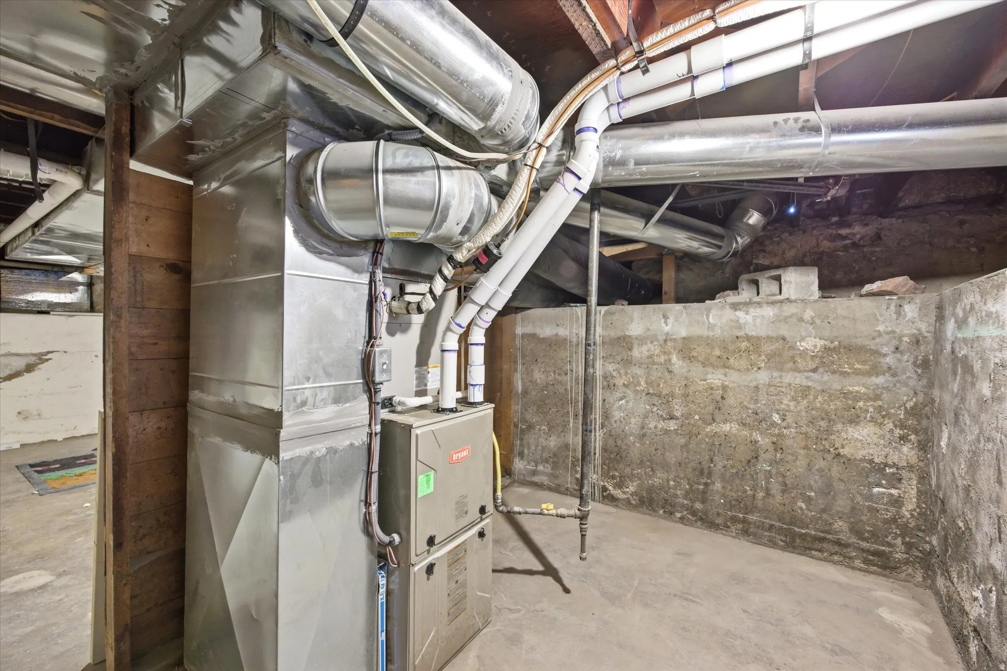 Basement utility area featuring a forced-air furnace unit with visible ductwork and exposed concrete walls