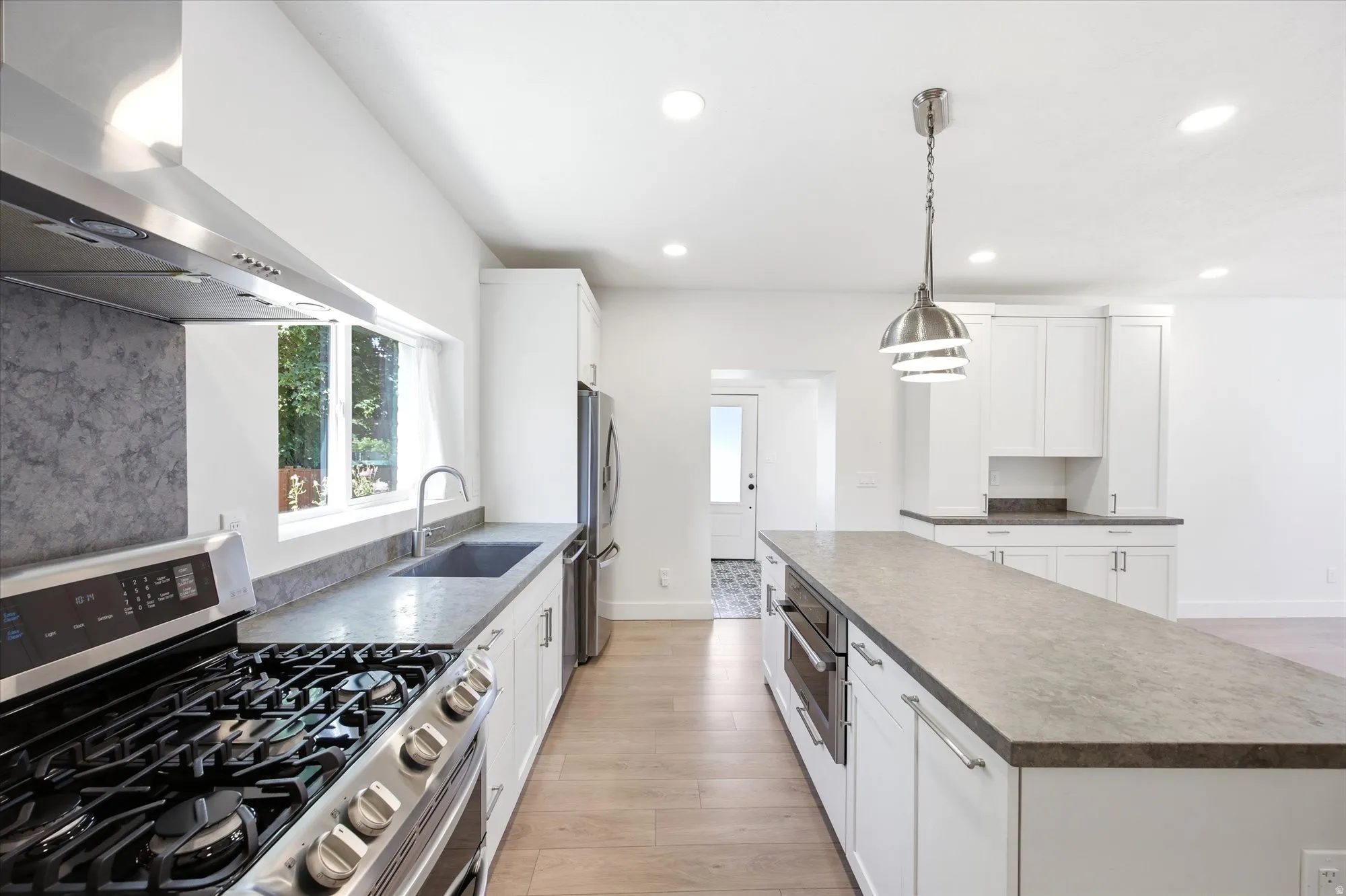 Modern kitchen featuring a large central island, stainless steel appliances, white cabinetry, recessed lighting, and wood-finish flooring