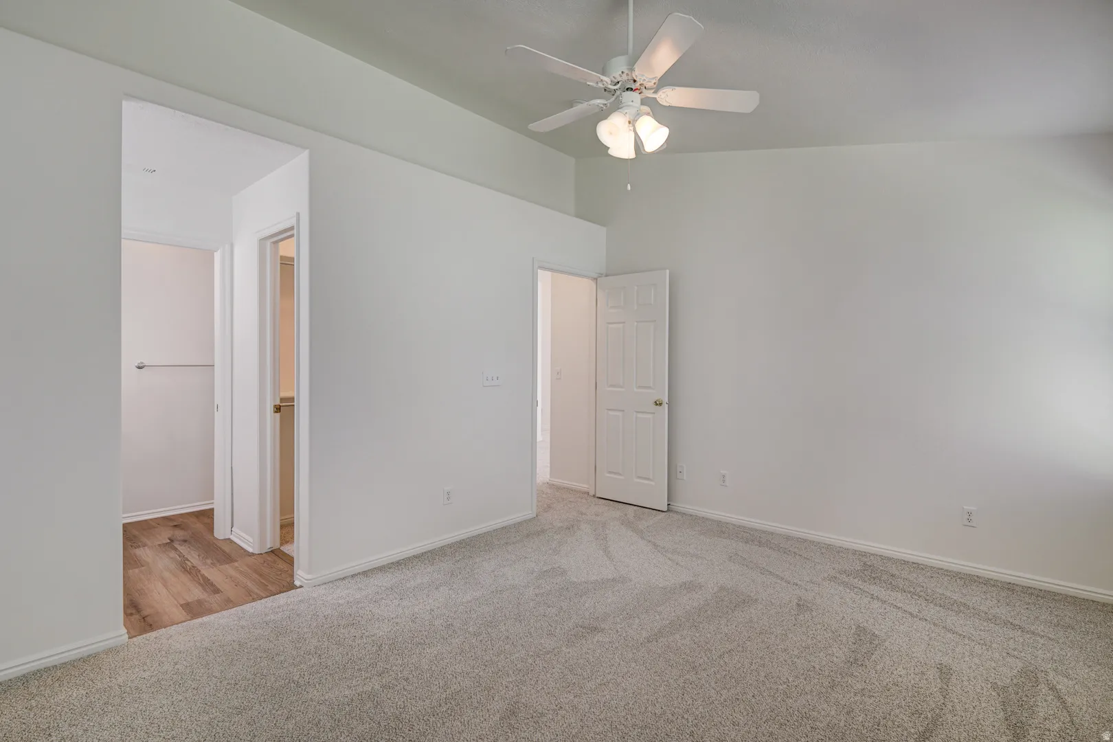Expansive primary suite featuring vaulted ceilings, a ceiling fan with integrated lighting, and light gray carpeting