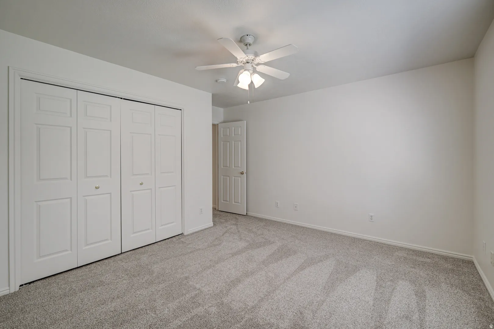 Bedroom featuring light carpet, white walls, bi-fold closet doors, and a ceiling fan with integrated lighting