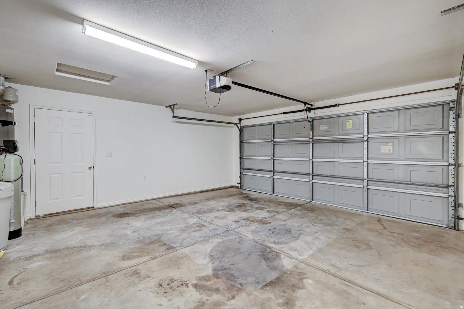 Spacious garage featuring an automatic garage door opener, white interior door, concrete flooring, and overhead fluorescent lighting