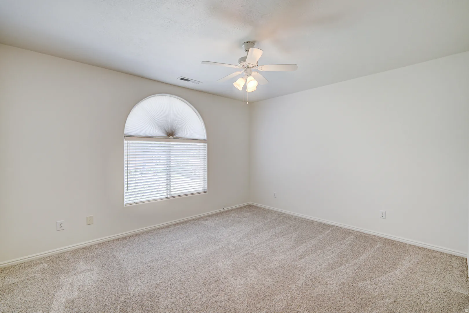 Spacious room featuring neutral carpeting, a large arched window with blinds, and a ceiling fan with integrated lighting