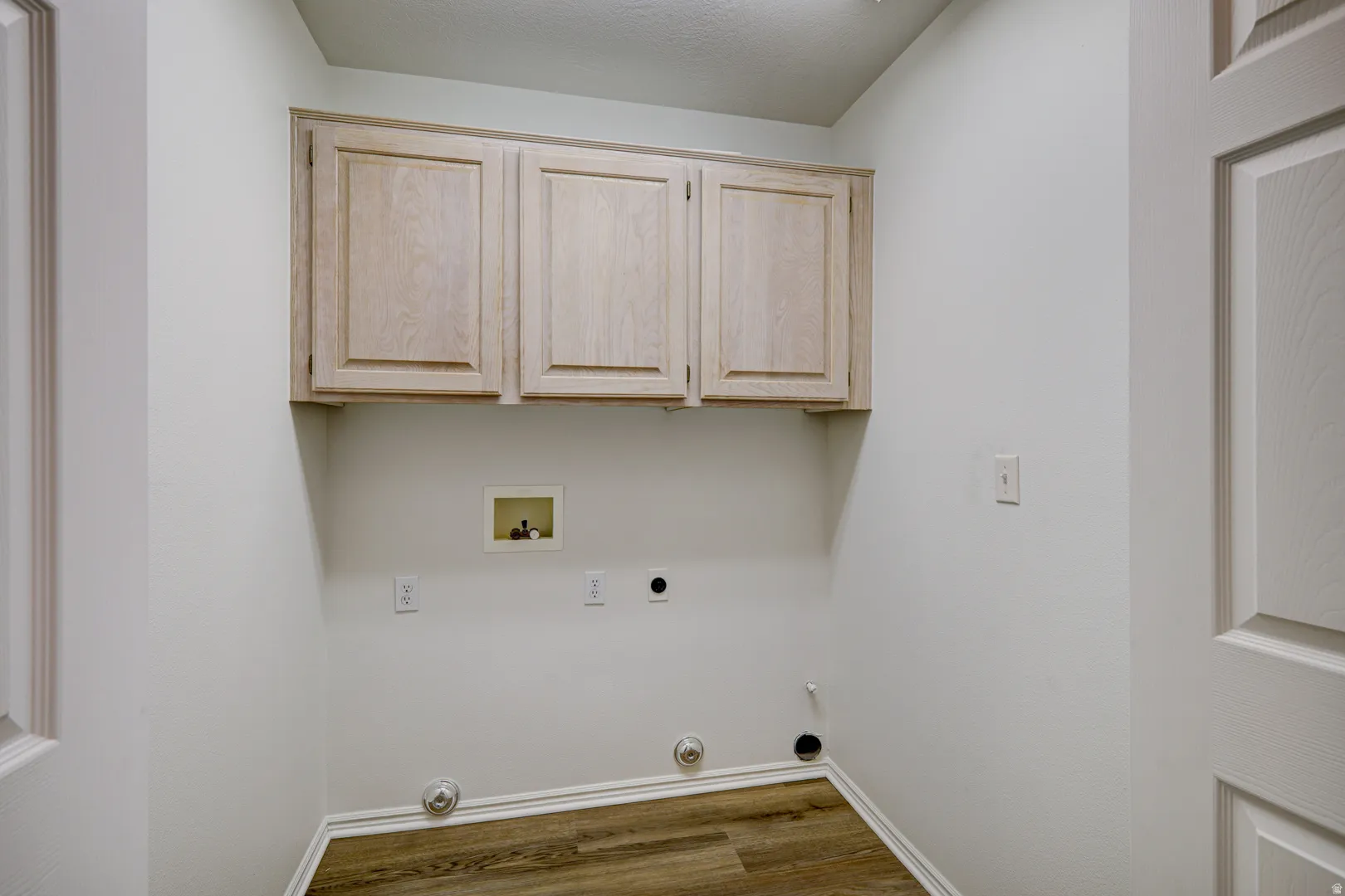 Laundry area featuring light-toned wood cabinetry, wood-finish flooring, and light-colored walls