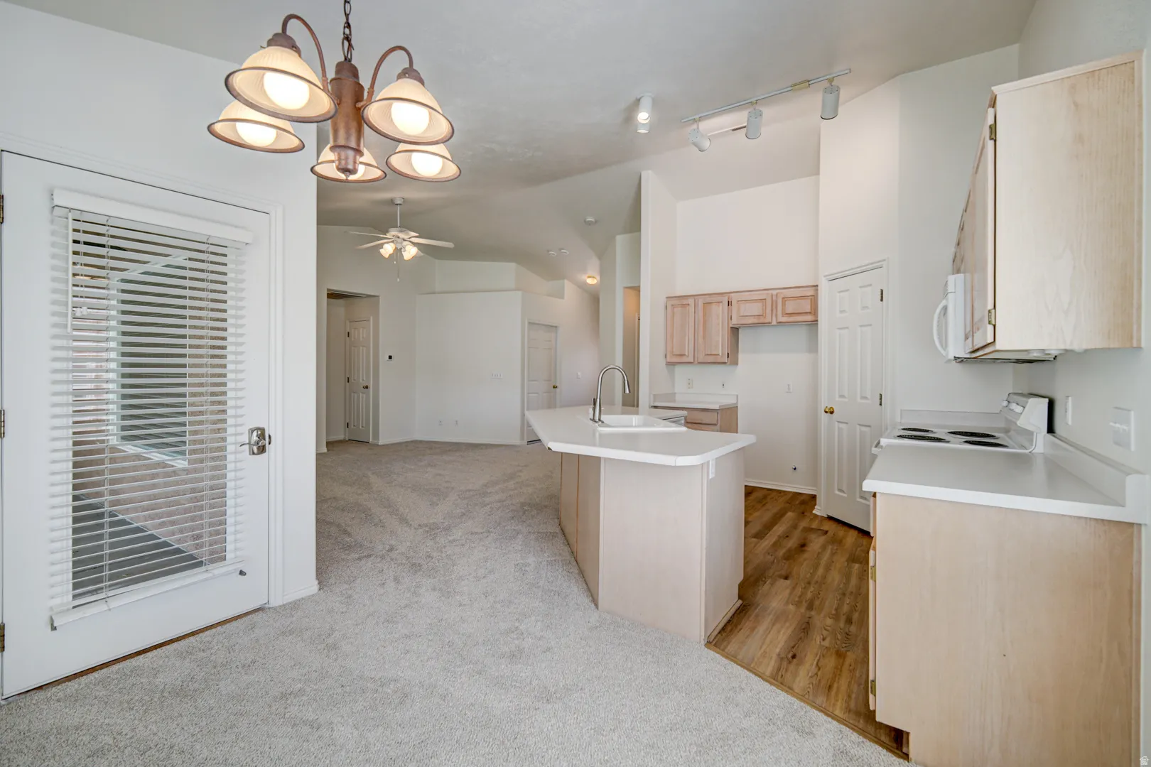 Kitchen and dining area featuring light wood-finish cabinetry, white countertops, a central island with an integrated sink, and an electric range