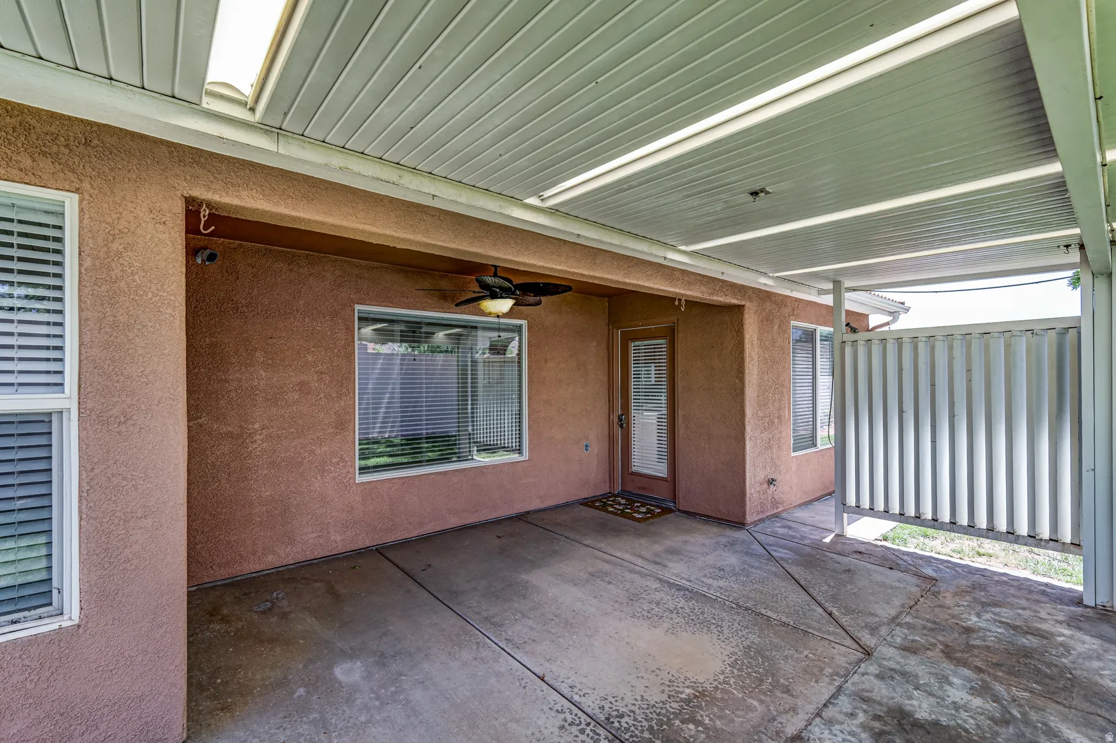 Covered patio with textured stucco walls, concrete flooring, overhead lighting, and a ceiling fan