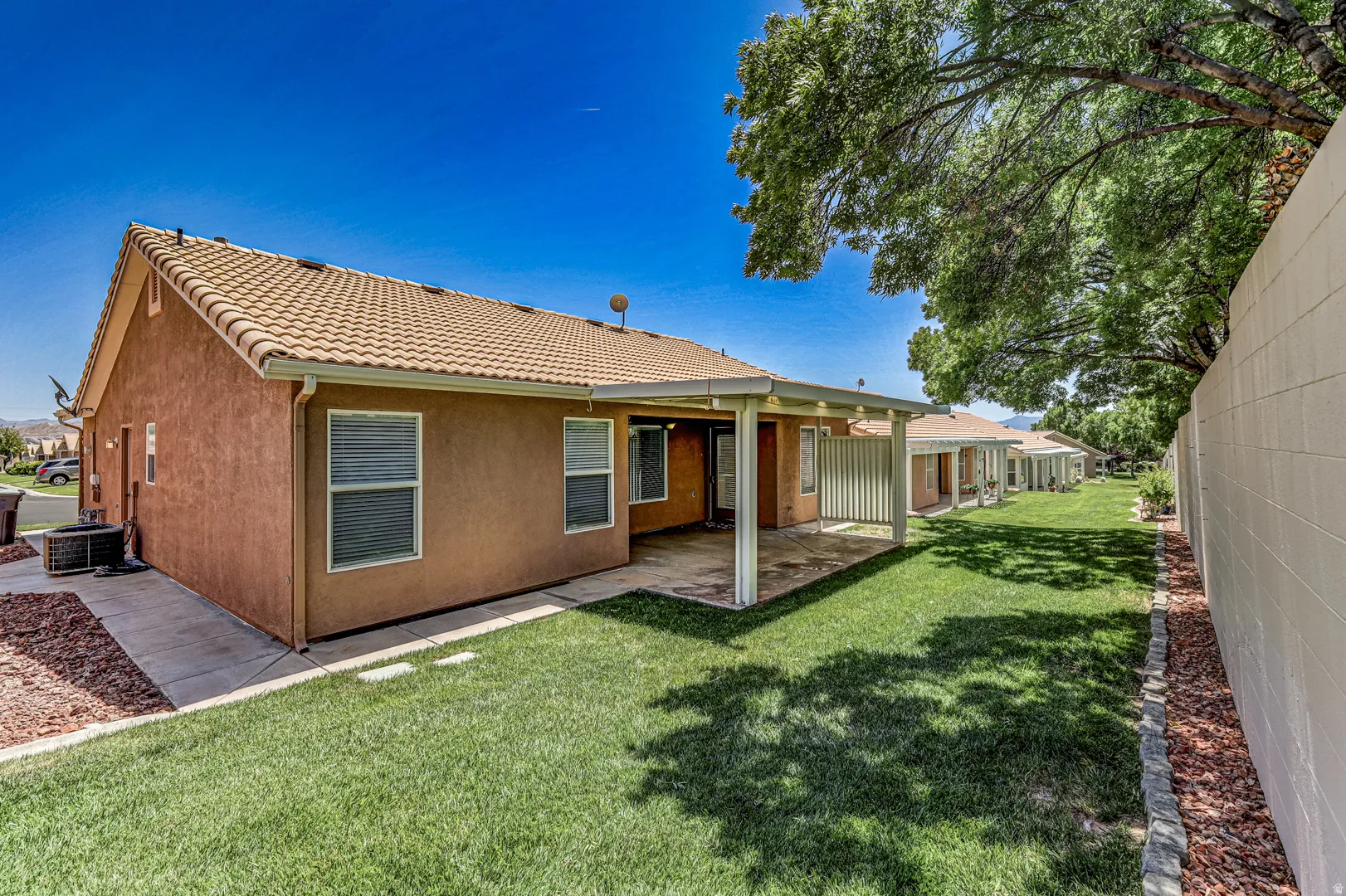 Exterior stucco finish with a tiled roof and covered patio overlooking a manicured lawn