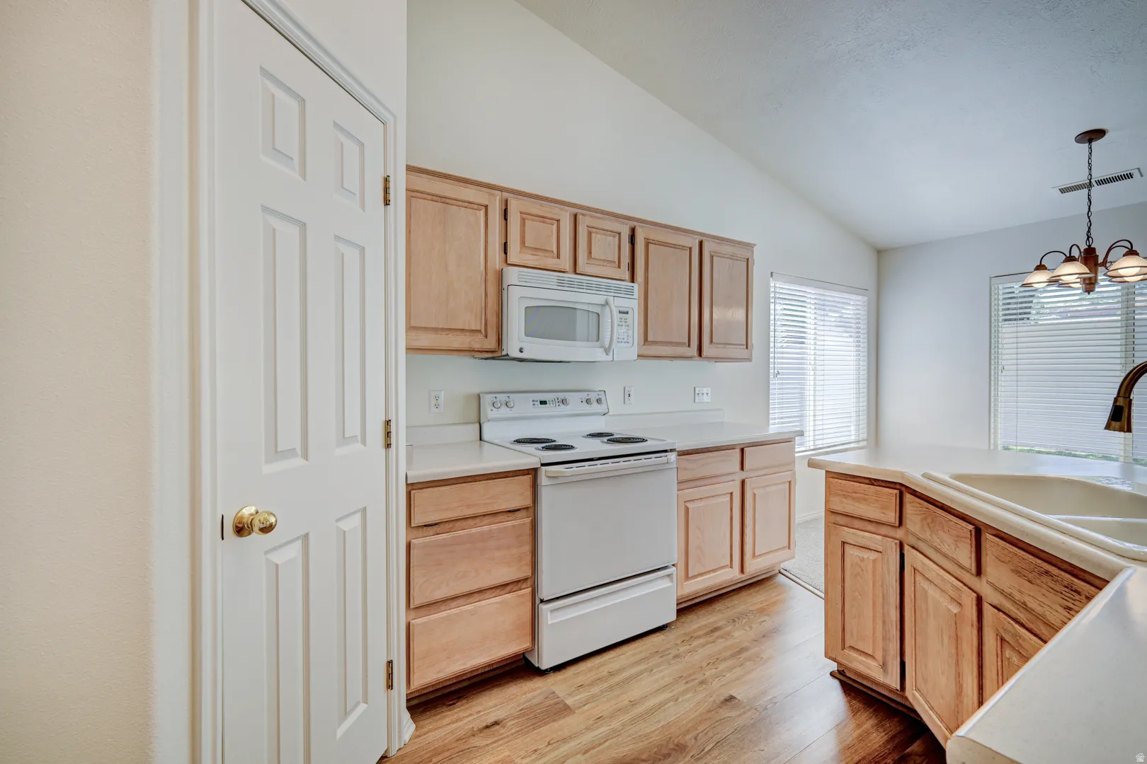 Kitchen featuring wood-finish flooring, light wood cabinetry, white countertops, and white appliances
