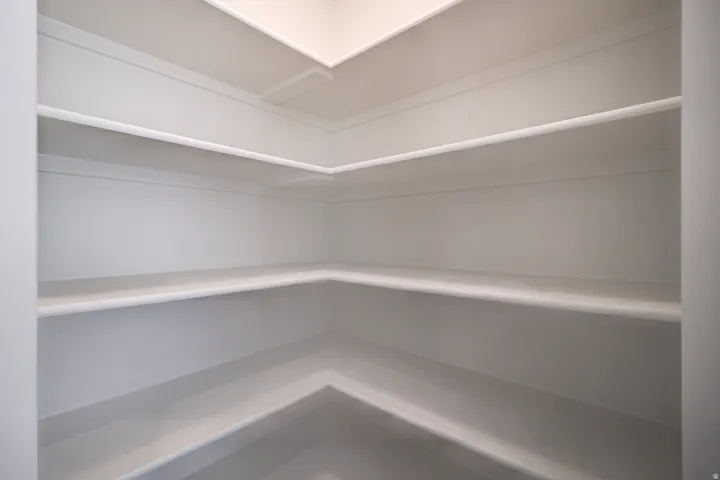 Walk-in pantry featuring multiple levels of built-in shelving, white painted finishes, and corner storage