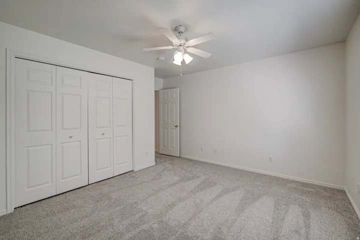 Bedroom featuring light carpet, white walls, bi-fold closet doors, and a ceiling fan with integrated lighting