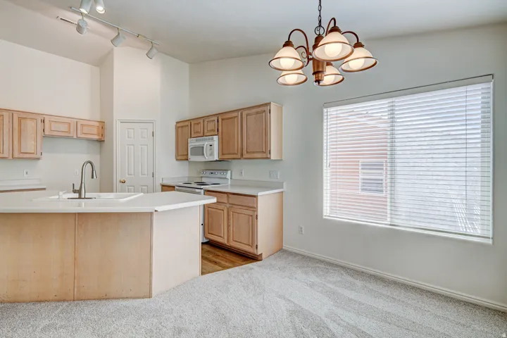 Open-concept kitchen and dining area featuring light wood cabinetry, a central island with an integrated sink, white appliances, and a window with blinds