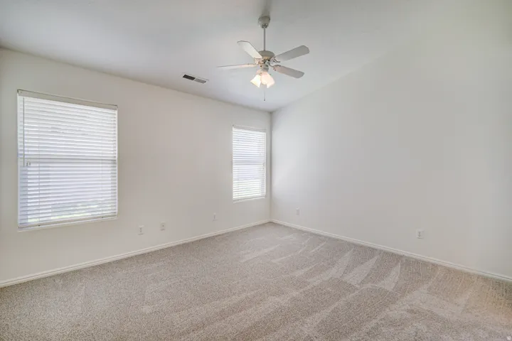 Spacious Primary Suite featuring neutral carpet flooring, white walls, two windows with blinds, a ceiling fan with light fixture, and vaulted ceilings
