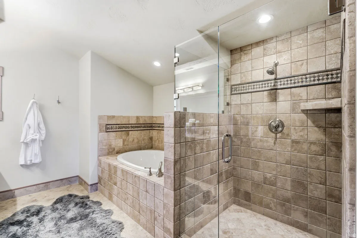 Tiled bathroom featuring a glass-enclosed shower with built-in shelf, a deep soaking tub with surrounding tile, and recessed lighting