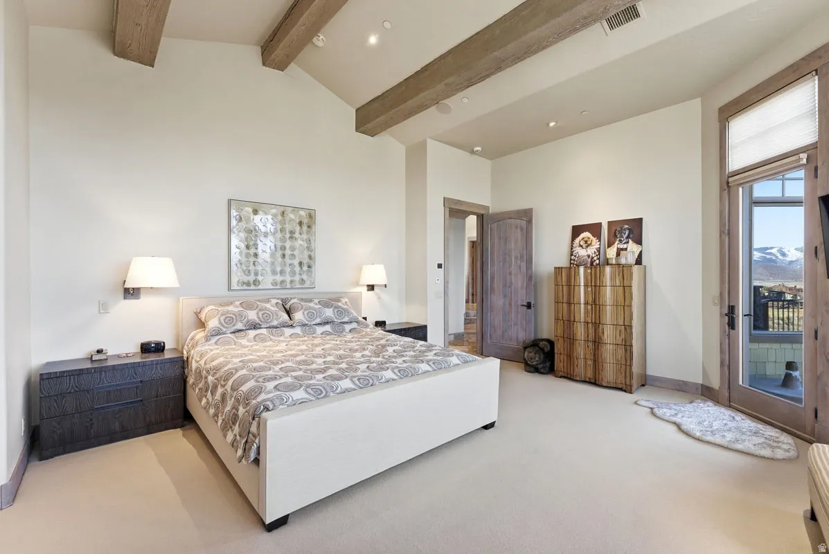 Vaulted ceiling with exposed wood beams, wall-mounted sconces, recessed lighting, wood-finish flooring, and a glass-paneled door leading to an outdoor space with mountain scenery