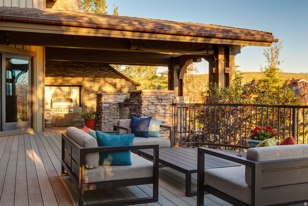Expansive outdoor deck featuring wood-finish flooring and a stone-clad outdoor kitchen area with a built-in grill