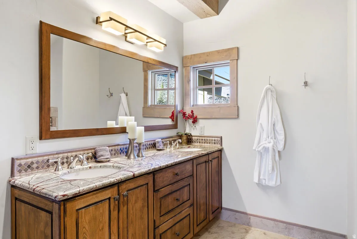 Double vanity featuring a light-colored countertop with integrated sinks, rich wood-finish cabinetry, and a mosaic tile backsplash