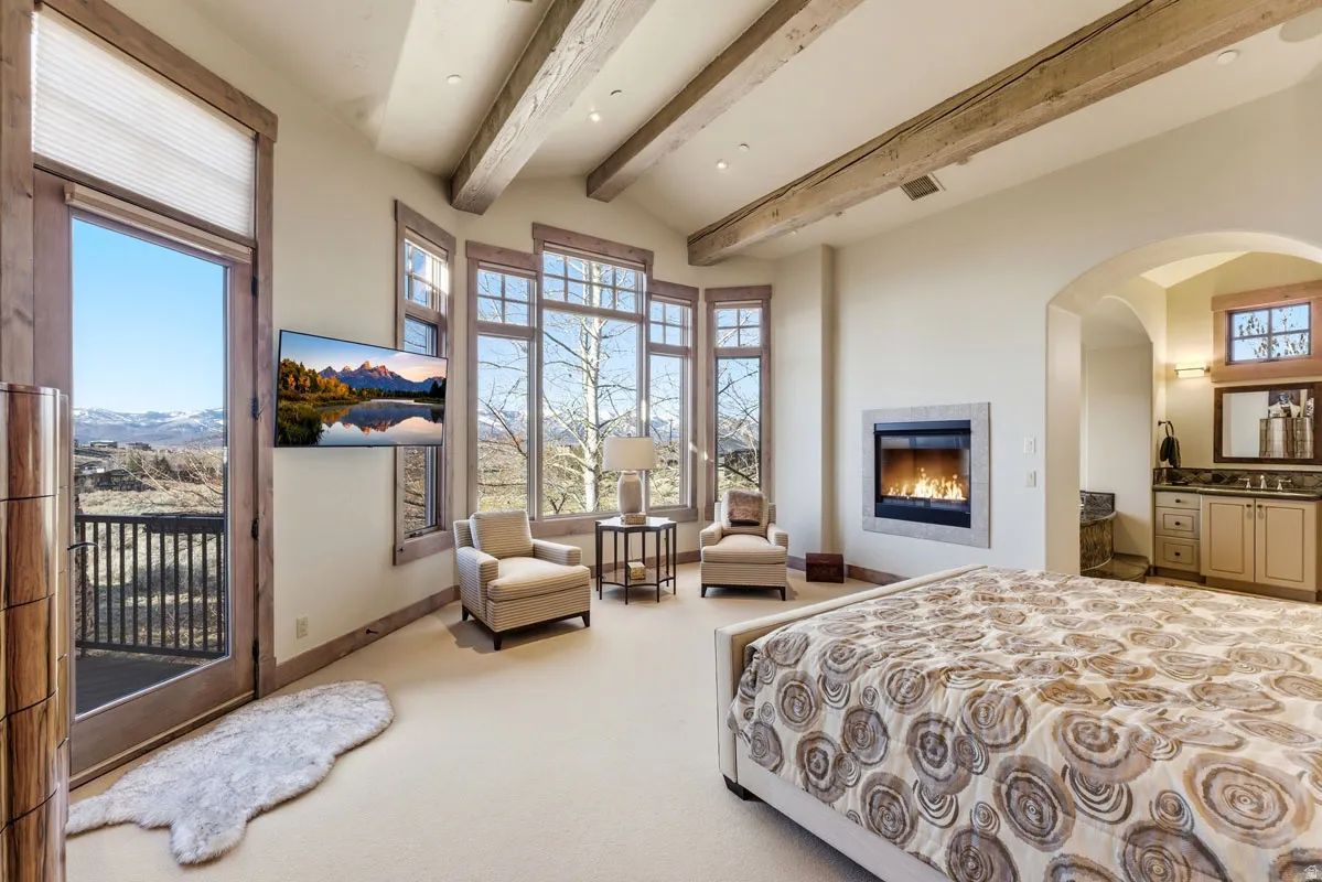 Vaulted ceiling with exposed wood beams, a built-in fireplace, a bay window feature, a built-in media console, and a private balcony