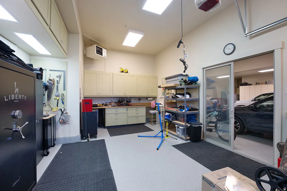 Spacious garage with light-colored epoxy flooring, extensive built-in cabinetry, overhead lighting, and a sliding glass door