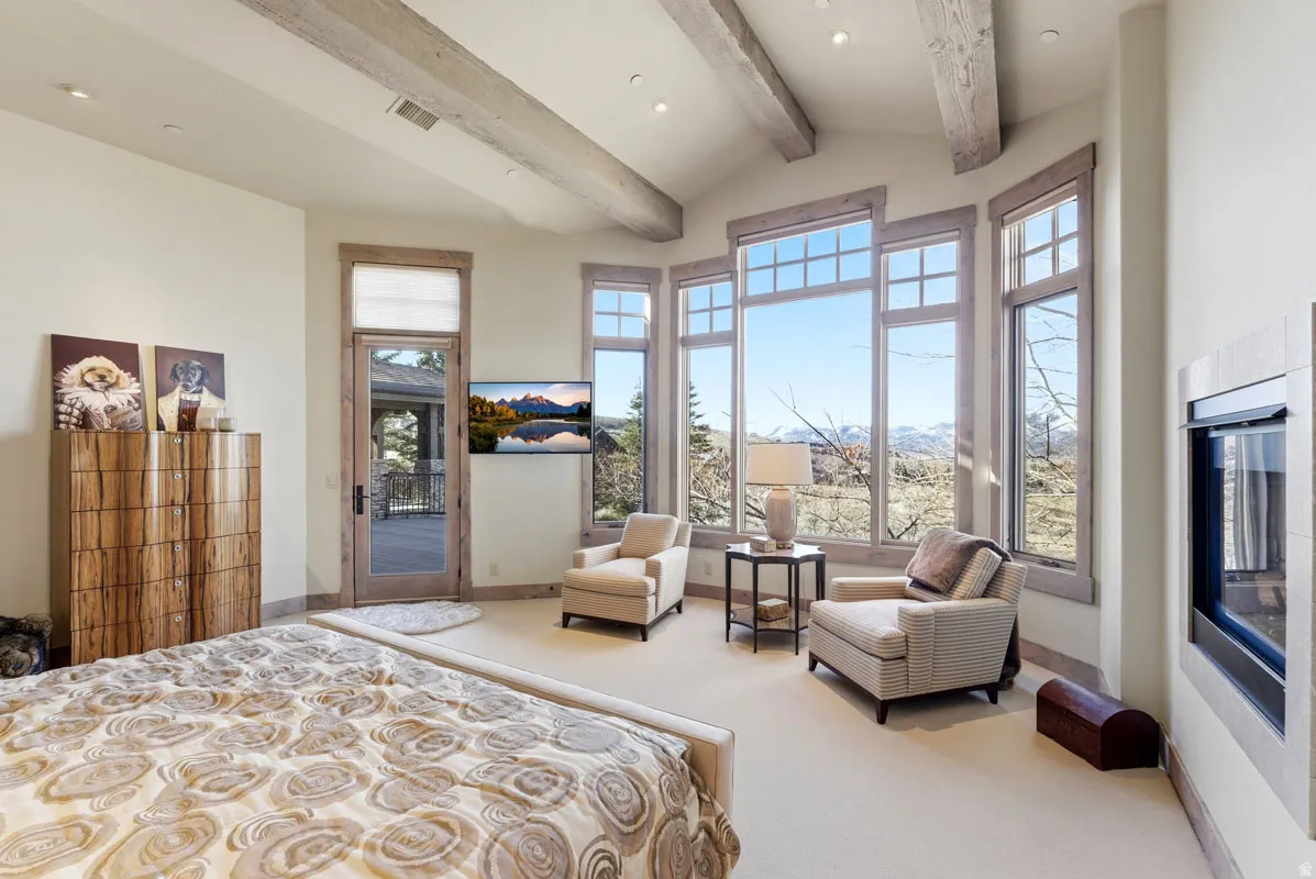 Vaulted ceiling with exposed wood beams, expansive window array, built-in fireplace, recessed lighting, and a glass-paneled exterior door