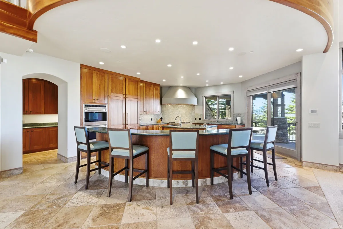 Gourmet kitchen featuring a large curved island with seating, extensive wood cabinetry, stainless steel appliances, and stone tile flooring