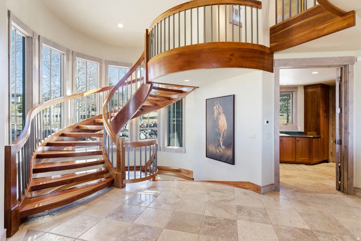 Curved hardwood staircase with metal balusters, illuminated by abundant natural light from a wall of windows